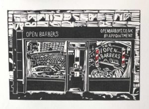 A black and white lino print of the shop front of Open Barbers. The barbers poles in the Open Barbers logo on the window are red and white, the only part of the print with colour. The shop front signage says Open Barbers on the left and openbarbers.co.uk on the right, with by appointment written underneath. The logo on the window includes the words Open Barbers. The windows capture reflections from the street inncluding brick buildings, a car and a bicycle.