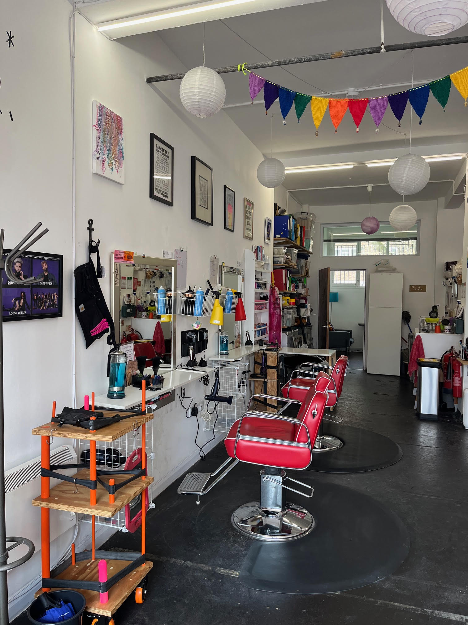 An interior view of Open Out with red styling chairs, a hairdressing set up, rainbow bunting and pictures on the walls.