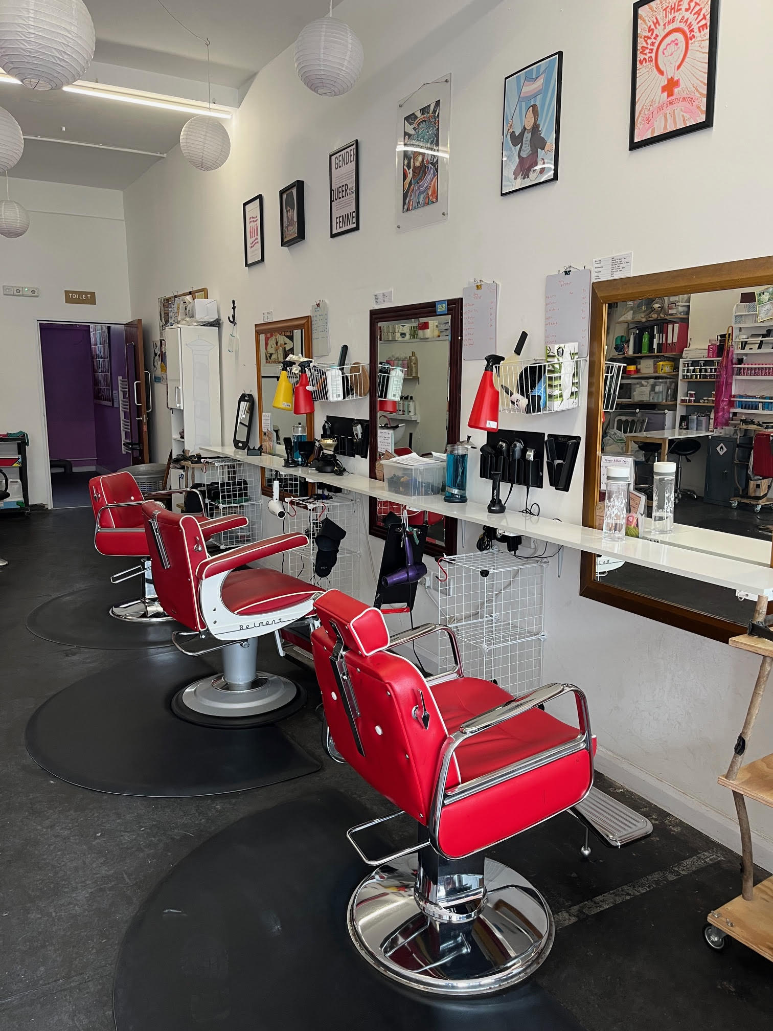 An interior view of Open Out with red styling chairs, a hairdressing set up and pictures on the walls.