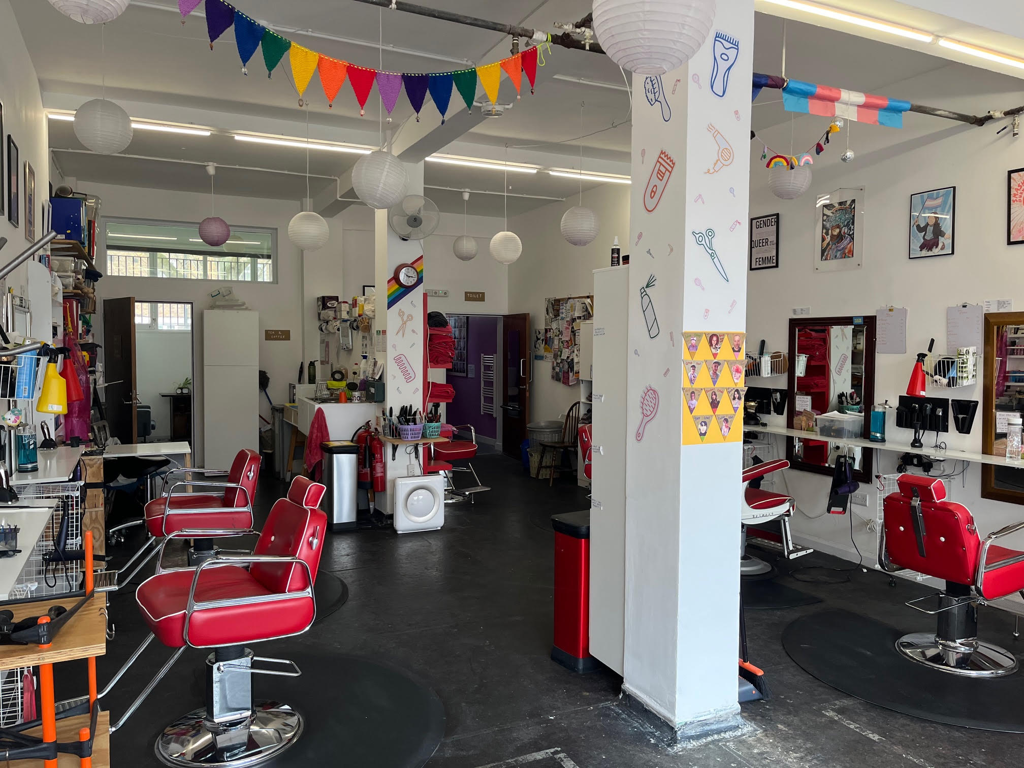An interior view of Open Out with red styling chairs, a hairdressing set up and pictures on the walls.